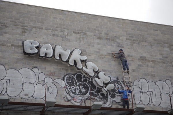 Men attempt to steal the Banksy! balloons in Queens. Photo via Animal New York.