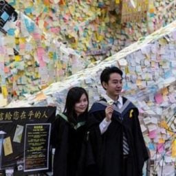 Students wearing graduation gowns pose for a photo in front of Hong Kong's pro-democracy "Lennon Wall." Photo: AFP.