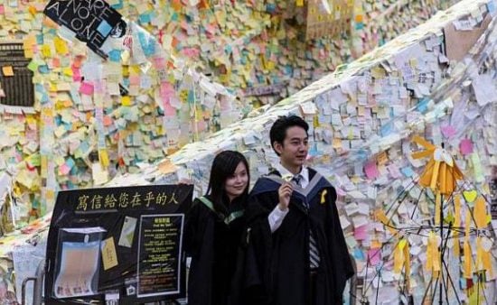 Students wearing graduation gowns pose for a photo in front of Hong Kong's pro-democracy 