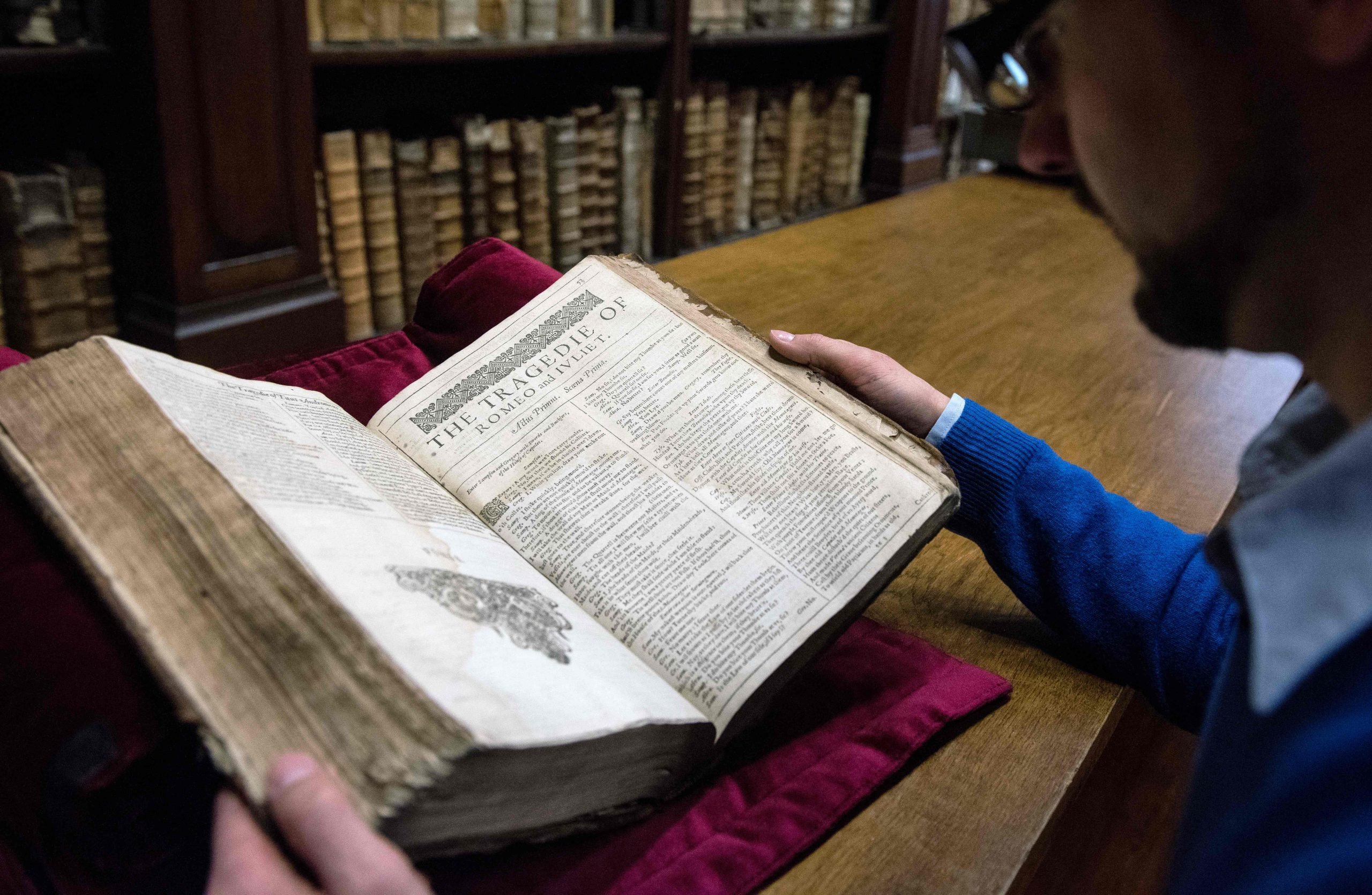 A man holding open a large book to a page headlined "The Tragedie of Romeo and Juliet."