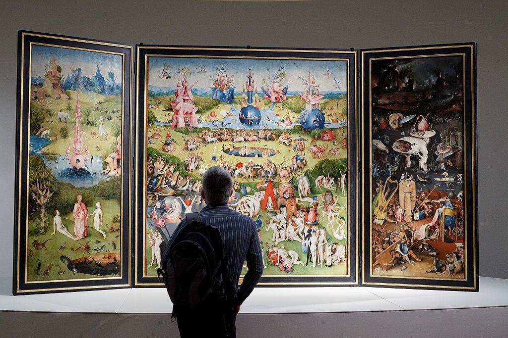 A man looks at of 'The Garden of Earthly Delights Triptych' by the Dutch painter Hieronymus Bosch. Photo by Pablo Blazquez Dominguez/Getty Images.​