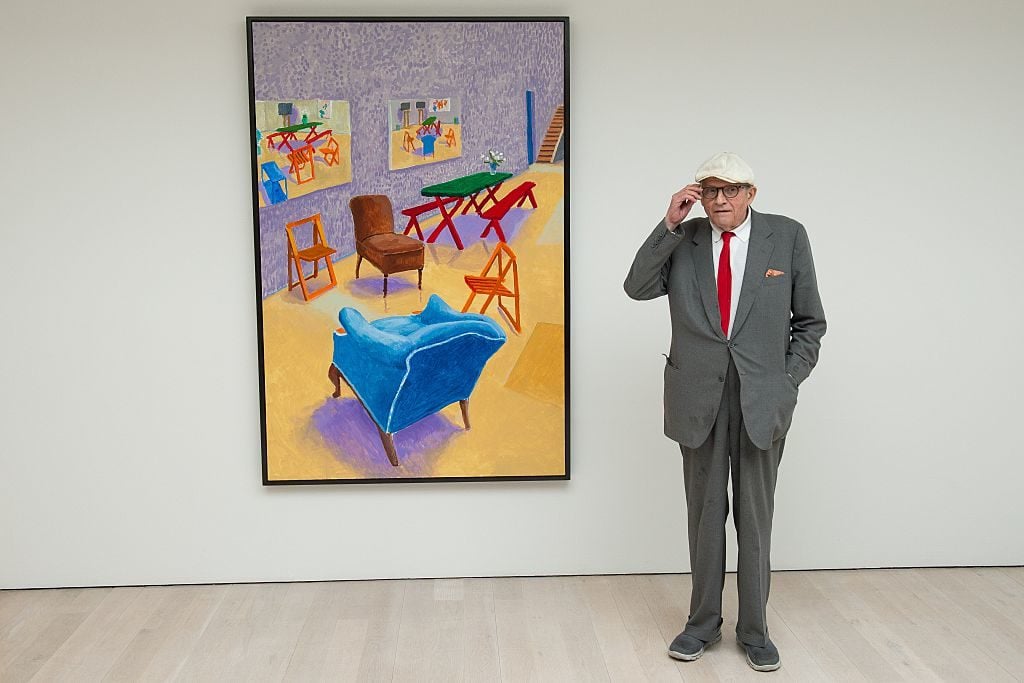 Artist David Hockney poses with his painting "Studio Interior #4 2014-2015." Photo credit LEON NEAL/AFP/Getty Images.