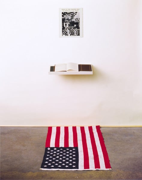 Dread Scott, What is the Proper Way to Display a US Flag?, 1988; Silver gelatin print, US flag, book, pen, shelf, audience.<br>Photo via DreadScott.net.