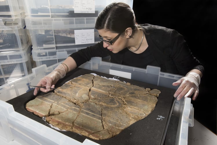 MOLA archaeological conservator Luisa Duarte examines a section of decorated Roman wall the 1st century AD discovered in London.<br>Photo: © MOLA.