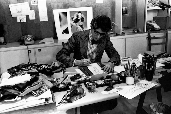 Yves Saint Laurent at his desk in 1976.<br>Photo: © Fondation Pierre Bergé – Yves Saint Laurent, Paris/ Guy Marineau.