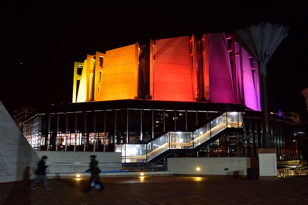 The Michael Fowler Centre is lit in rainbow colors by the city council during a candle lit vigil across the road at Frank Kits Park in Wellington on June 13, 2016, in remembrance of victims after a gunman opened fire in a gay nightclub in Orlando, Florida in the worst mass shooting in US history. Courtesy photographer Marty Melville/AFP/Getty Images.
