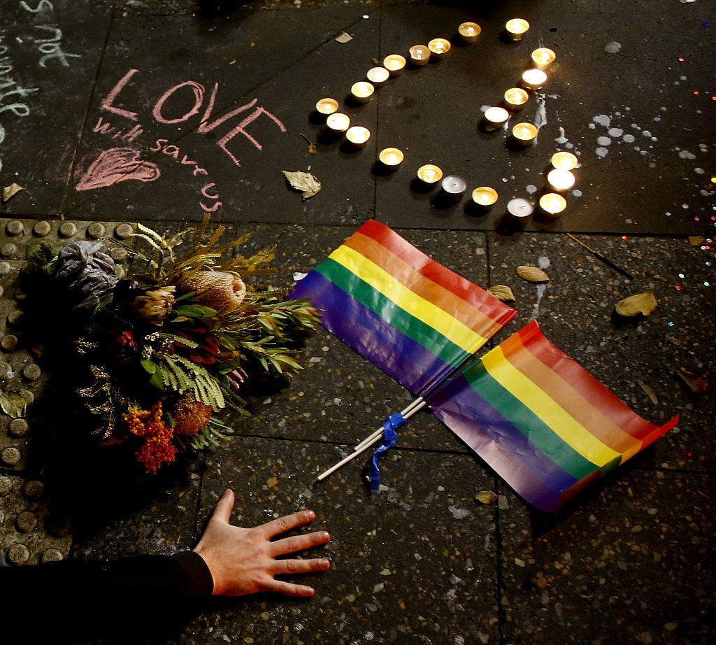 SYDNEY, AUSTRALIA - JUNE 13: A man touches the ground next to rainbow flags during a candlelight vigil for the victims of the Pulse Nightclub shooting in Orlando, Florida, at Newtown Neighbourhood Centre on June 13, 2016 in Sydney, Australia. 50 people were killed and 53 injured after a gunman opened fire on people in a gay nightclub in Florida. It is the deadliest mass shooting in US history. (Photo by Daniel Munoz/Getty Images)