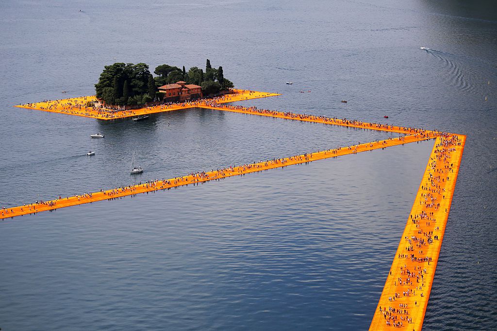 People walk on the monumental installation entitled 'The Floating Piers' created by artist Christo Vladimirov Javacheff on Iseo Lake, in northern Italy, on June 18, 2016. Some 200,000 floating cubes create a 3-kilometers runway connecting the village of Sulzano to the small island of Monte Isola on the Iseo Lake for a 16-day outdoor installation opening today. Courtesy of MARCO BERTORELLO/AFP/Getty Images.