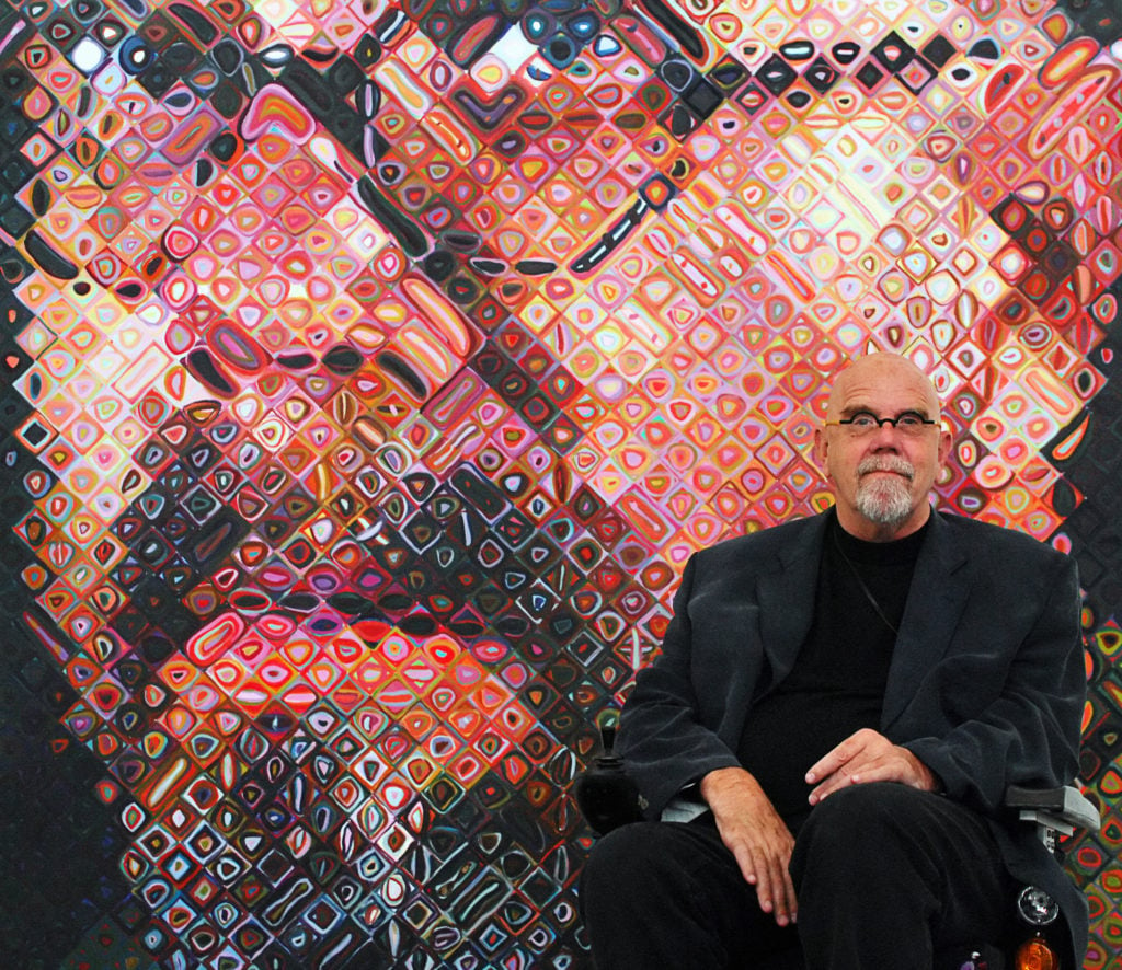 Chuck Close sits in front of his painting. Courtesy of Getty Images.