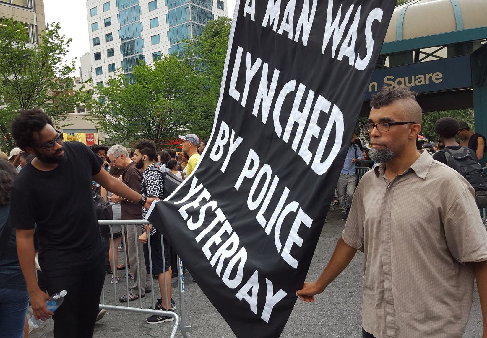 Dread Scott with flag, A Man Was Lynched By Police Yesterday. Courtesy of Connie Julian via Facebook.