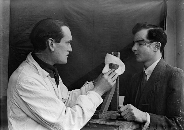 Captain Francis Derwent Wood RA of the Royal Army Medical Corps holds an artist’s palette as he adds the finishing touches to a patient’s new facial plate Photo by Horace Nicholls, c1914–8 © IWM, courtesy the Imperial War Museum, London, originally from the Ministry of Information collection titled The Development of Reconstructive Plastic.