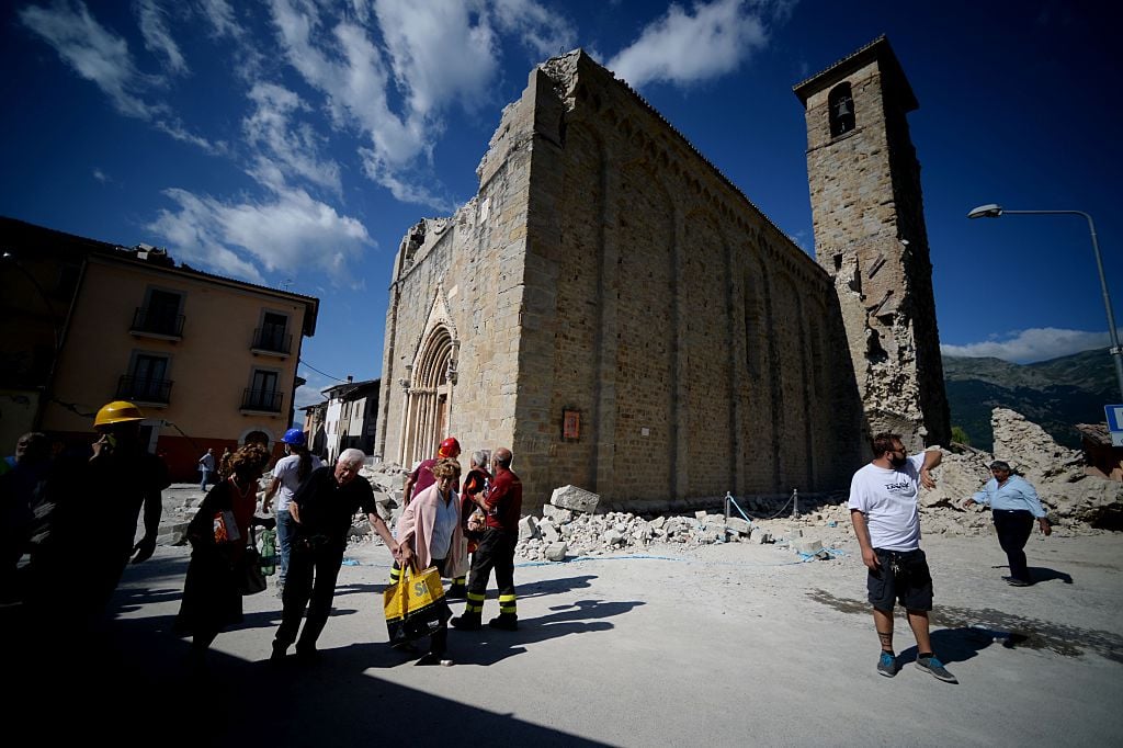People walk past an earthquake damaged church during search and rescue operations in Amatrice on August 24, 2016 after a powerful earthquake rocked central Italy. Photo Filipo Monteforte/AFP/Getty Images.