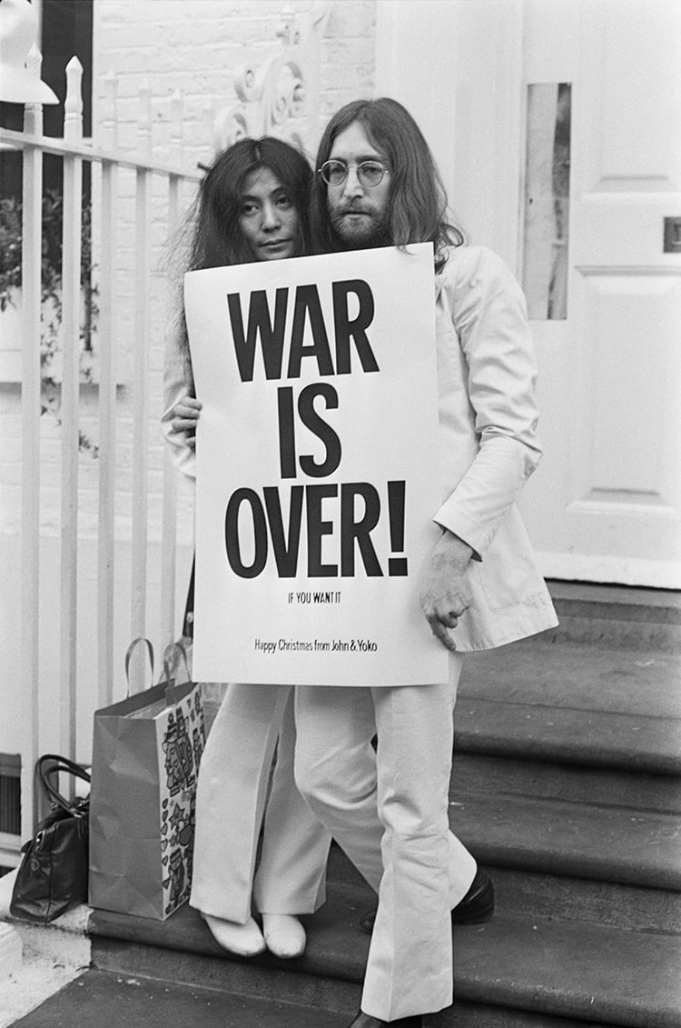John Lennon and Yoko Ono pose on the steps of the Apple building in London, holding one of the posters that they distributed to the world's major cities as part of a peace campaign protesting against the Vietnam War, December 1969. Courtesy of Frank Barratt/Keystone/Getty Images.