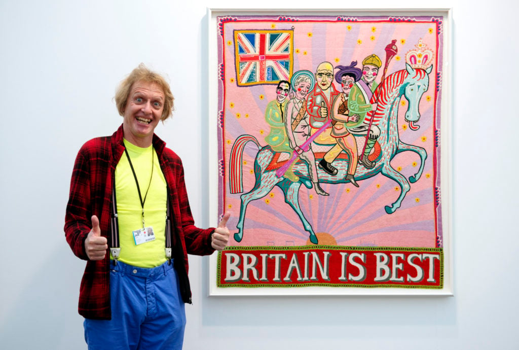 Grayson Perry poses in front of one his works at the Victoria Miro booth at Frieze London 2016. Photo by Linda Nylind, courtesy of Linda Nylind/Frieze.