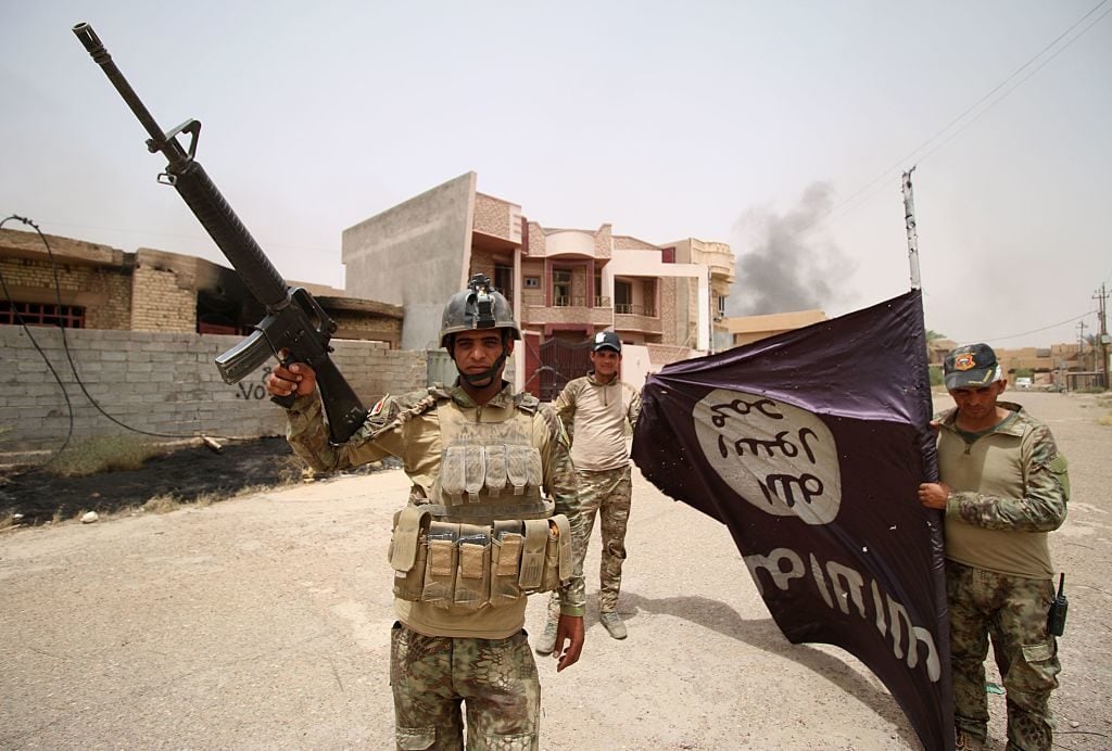 Iraqi pro-government forces hold an Islamic State (IS) group flag in Fallujah as they try to clear the city of IS fighters on June 19, 2016. Photo Haidar Mohammmed Ali/AFP/Getty Images.