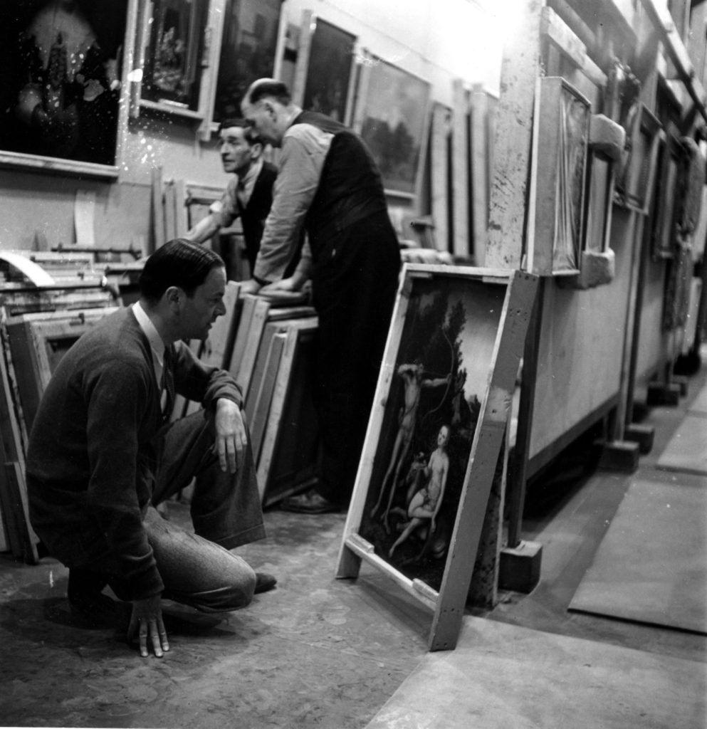 20th October 1942: Sir Kenneth Clark (1903 -1983), director of the National Gallery, closely examines a painting from the Royal Collection, Cranach's 'Adam and Eve', to see if it is in need of restoration. Photo Fred Ramage/Keystone Features/Getty Images.