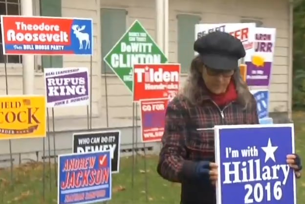 Nina Katchadourian adds a Hillary Clinton sign to her piece <em>Monument to the Unelected</em> following Donald Trump's unexpected win. Screenshot from News 12, via YouTube. 