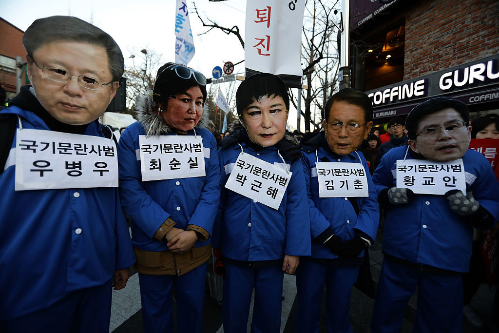 Protesters in Seoul on December 10, 2016 wear masks of the faces of Choi Soon-Sil (center left) and Park Geun-Hye (center right). As the president awaits trial for impeachment, prosecutors begin to investigate an alleged artist blacklist of 9,000 cultural figures. Photo courtesy Chung Sung-Jun/Getty Images.