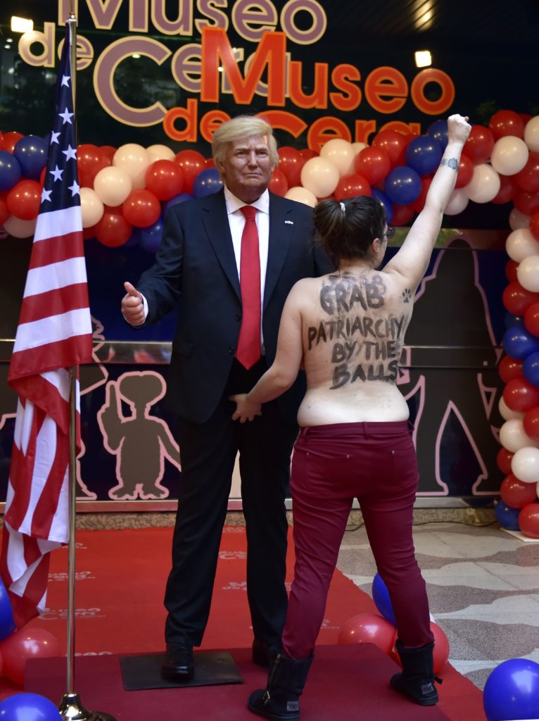 A topless Femen activist with a sign painted on her back raises her fist as she protests in front of a wax statue of US President-elect Donald Trump during its unveiling at the Wax Museum of Madrid. Courtesy of Gerard Julien/AFP/Getty Images.