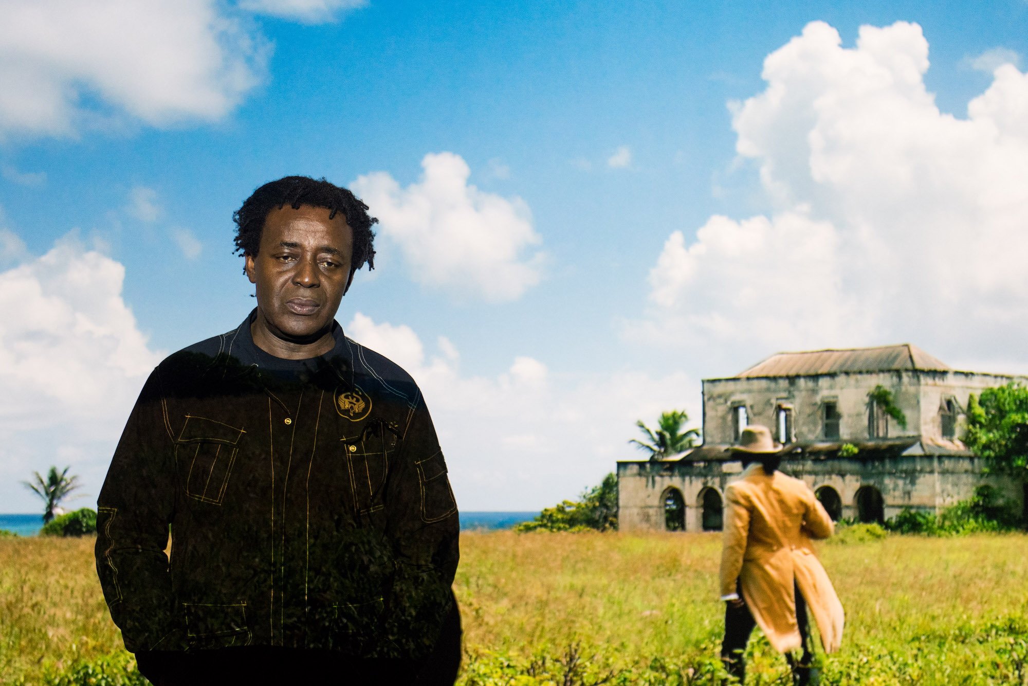 John Akomfrah, winner of Artes Mundi Prize 2017, poses in front of Auto Da Fé (2016) at the National Museum Cardiff. Photo Polly Thomas, courtesy Artes Mundi.