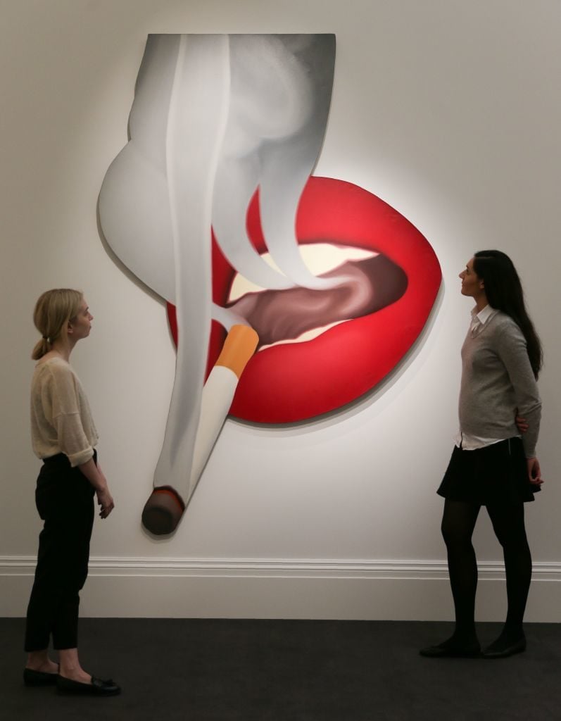 Employees pose with Tom Wesselmann's <i>Smoker #5 (mouth #19)</i>, at Sotheby's in 2017. Courtesy of DANIEL LEAL-OLIVAS/AFP/Getty Images.