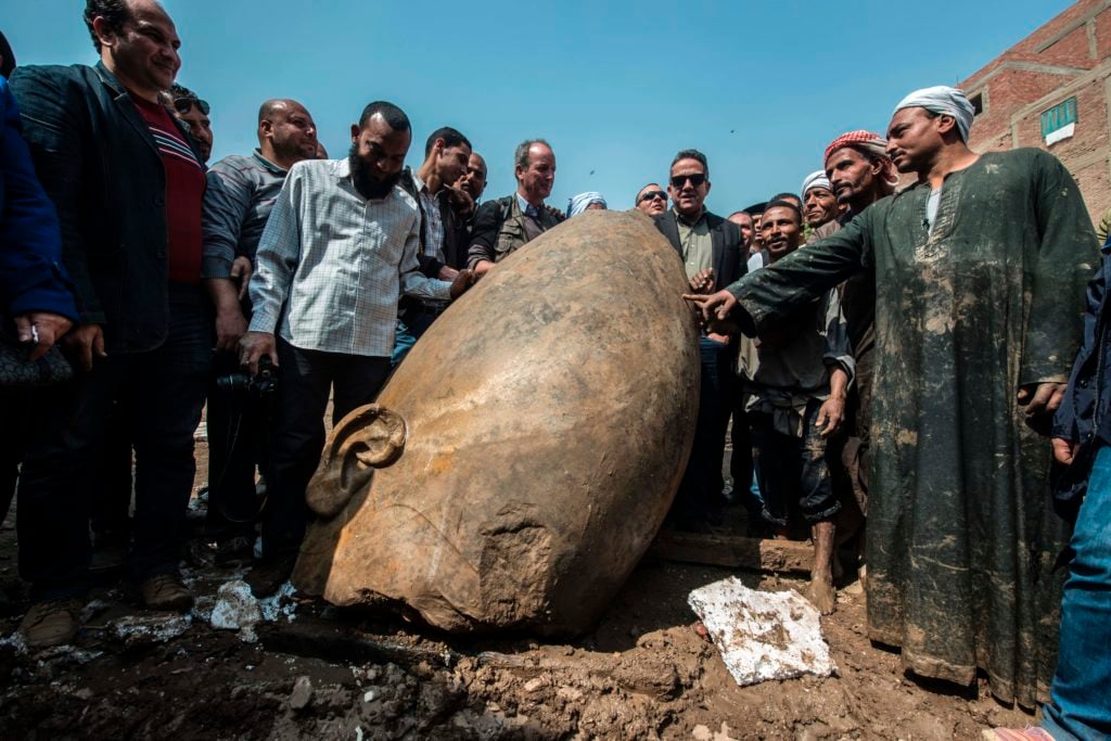 Egyptian minister of antiquities Khaled el-Anani poses for picture with workers next to the head of a statue at the site of a new discovery by a team of German-Egyptian archeologists in Cairo's Mattarya district on March 9, 2017. Courtesy of Khaled Desouki/AFP/Getty Images.