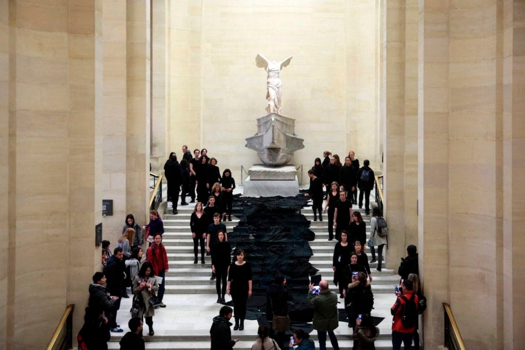 Members of the campaign collective “Libérons le Louvre” stand in front of the Winged Victory of Samothrace, during a performance to denounce the sponsor partnership between the museum and Total, at the Louvre on March 5, 2017. Photo GEOFFROY VAN DER HASSELT/AFP/Getty Images.