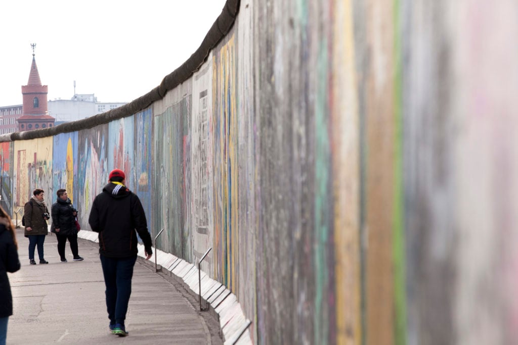 Visitors walk along the East Side Gallery, a mile-long section of the Berlin Wall still standing that is covered in murals and graffiti, on March 5, 2017 in Berlin, Germany. The work of 118 different artists from 21 countries is on display. Courtesy of Melanie Stetson Freeman/The Christian Science Monitor via Getty Images.