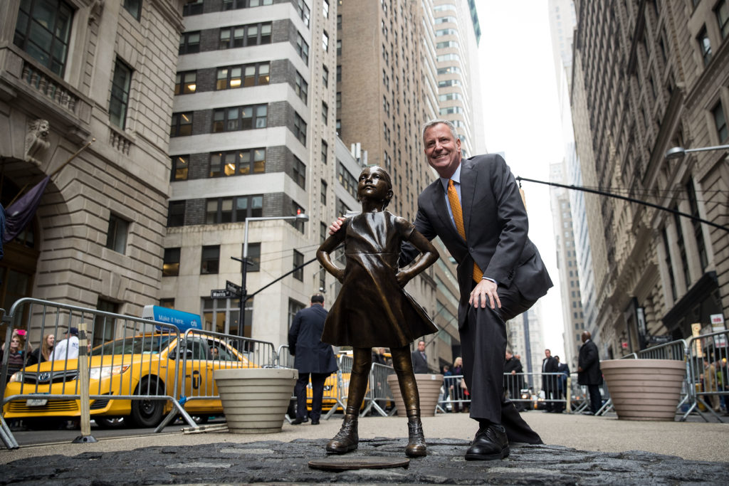 New York City Mayor Bill De Blasio poses for a photo with the Fearless Girl statue during a press availability, March 27, 2017 in New York City. Courtesy of Drew Angerer/Getty Images.
