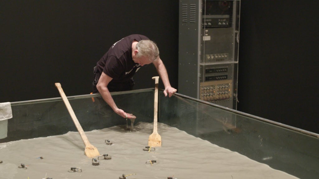 Still from "AT THE MUSEUM: Rauschenberg's Mud Muse – Part 1," courtesy The Museum of Modern Art, New York. Pictured: Gunnar Marklund, Technician at Moderna Museet with Robert Rauschenberg’s Mud Muse (1968–71). Bentonite mixed with water in aluminum-and-glass vat, with sound-activated compressed-air system and control console. Moderna Museet, Stockholm. Gift of the New York Collection. © 2017 Robert Rauschenberg Foundation