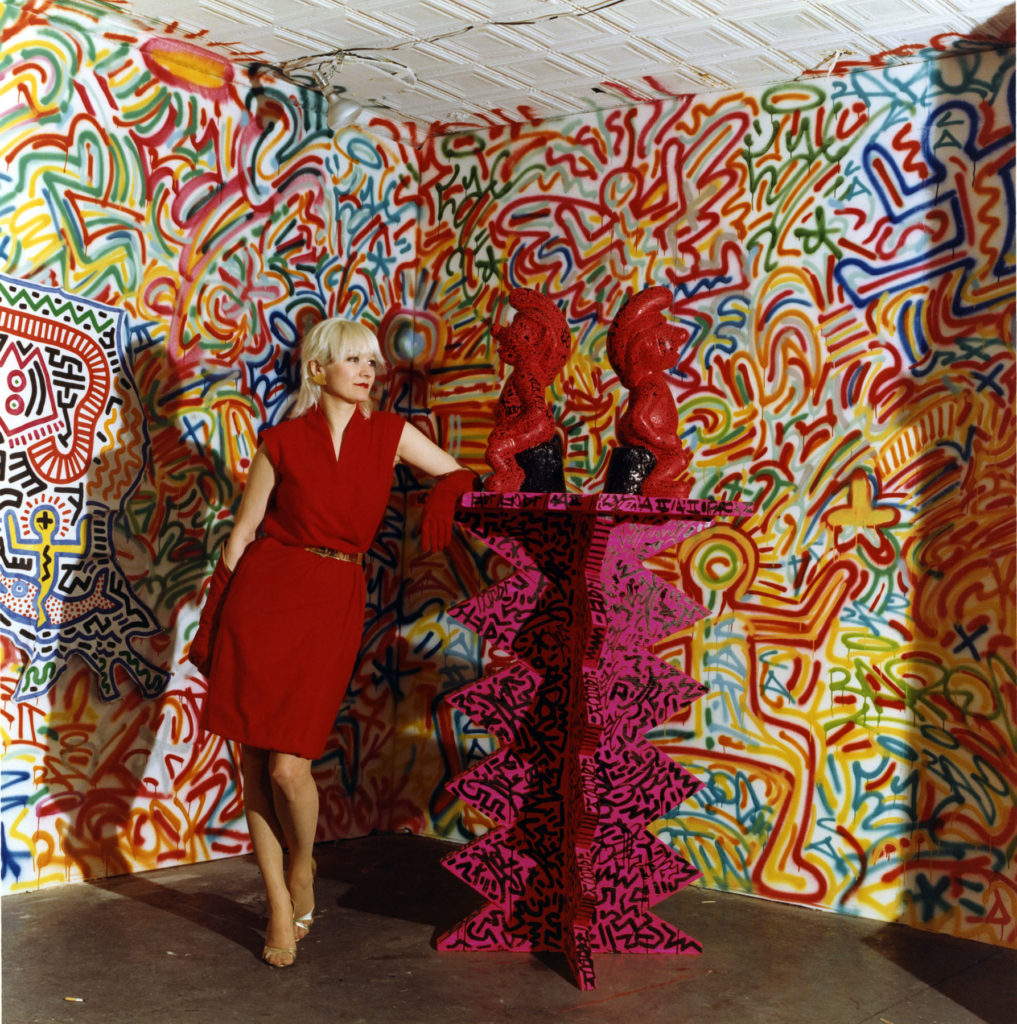 Patti Astor in February 1983 with Keith Haring’s The Smurfs and LA II. Courtesy of the Urban Art Fair/photographer Eric Kroll.