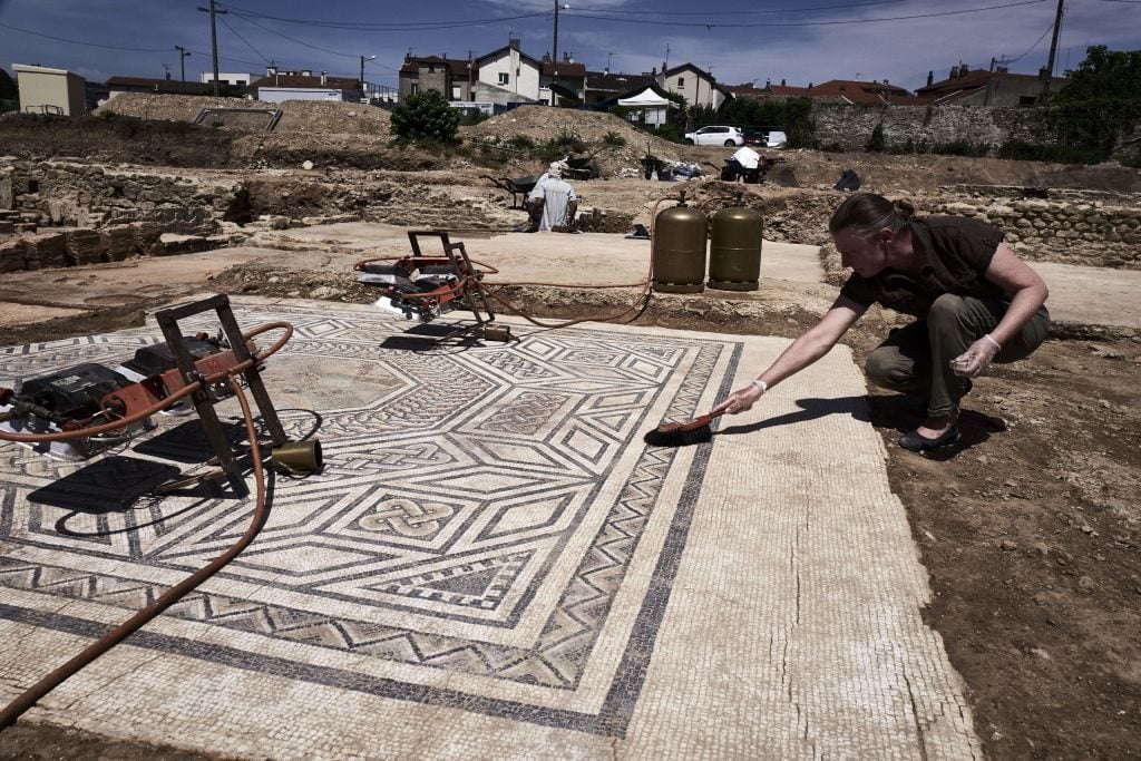 An archaeologist works on a mosaic on July 31, 2017, on the archaeological antiquity site of Sainte-Colombe, near Vienne, eastern France, where remains of an entire neighbourhood of the Roman city of Vienne have been uncovered. Photo JEAN-PHILIPPE KSIAZEK/AFP/Getty Images.