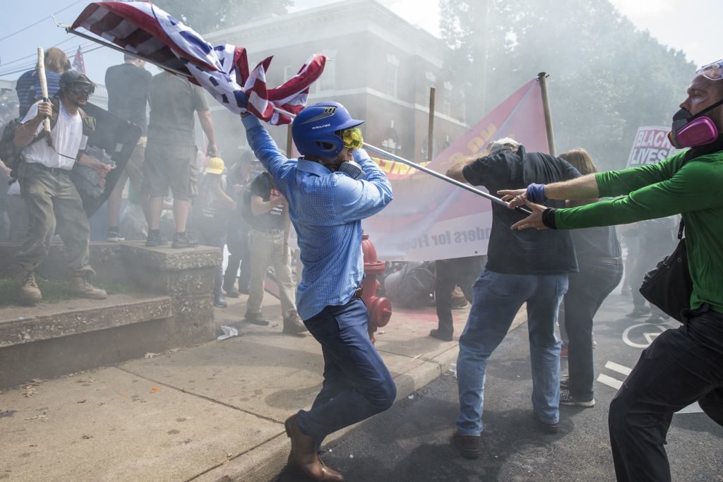 A White Supremacist tries to strike a counter protestor with a White Nationalist flag during clashes at Emancipation Park, where White Nationalists are protesting the removal of the Robert E. Lee monument in Charlottesville, Va. Photo by Samuel Corum/Anadolu Agency/Getty Images.