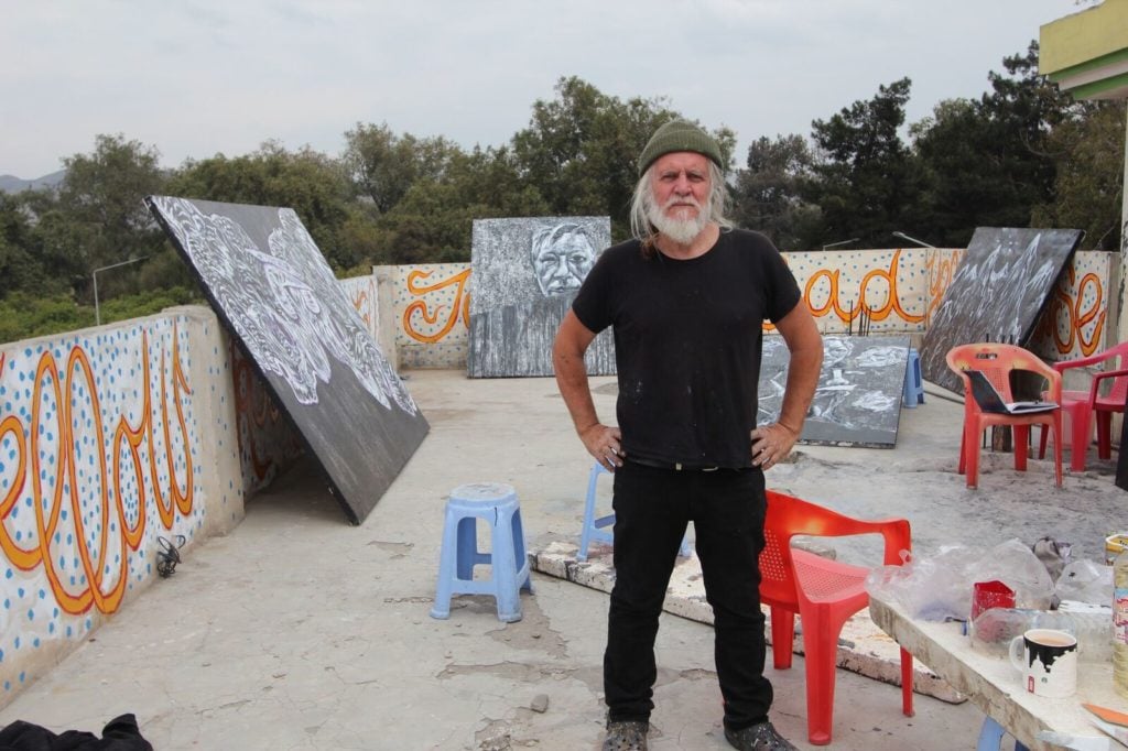 Artist George Gittoes with his paintings, including that of Julian Assange, on the roof of the Yellow House art center in Jalalabad, Afghanistan. Courtesy of the artist.