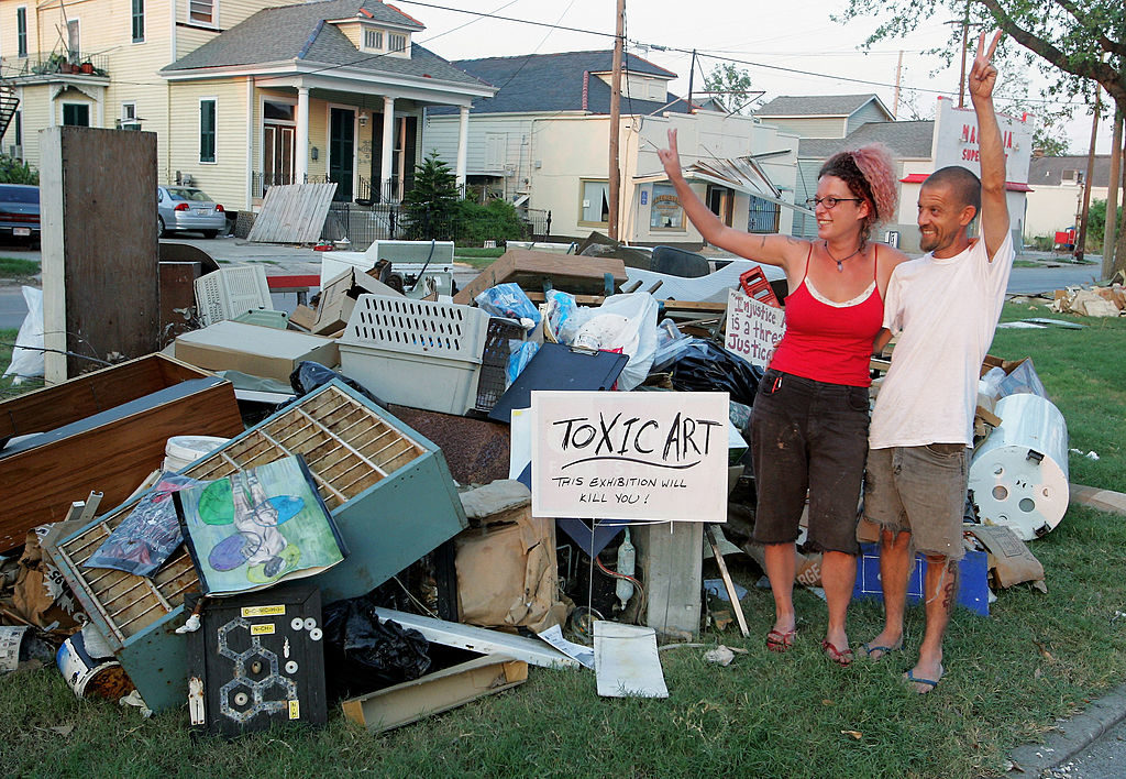 Artist Andrea Garland and her husband, artist Jeffrey Holmes, wave to passers-by as they pose by their display of damaged artwork in the median outside their home in the Upper Ninth Ward September 21, 2005 in New Orleans, Louisiana. Photo by Ethan Miller/Getty Images.