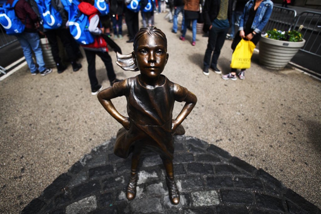 Kristen Visbal's Fearless Girl statue stands facing Arturo DiModica's iconic Charging Bull sculpture as tourists take pictures. DiModica alleges that Fearless Girl infringes upon his copyright, distorts his artistic message, and should be moved elsewhere. Courtesy of Jewel Samad/AFP/Getty Images.