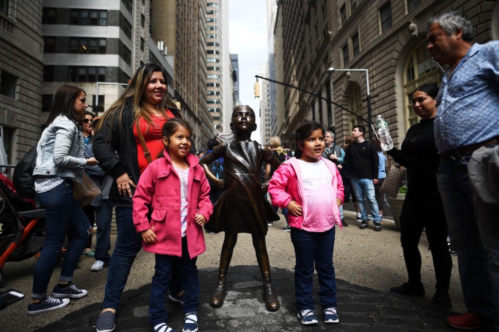 Kristen Visbal's <em>Fearless Girl</em> statue stands facing Arturo DiModica's iconic <em>Charging Bull</em> sculpture as tourists take pictures. DiModica alleges that <em>Fearless Girl</em> infringes upon his copyright, distorts his artistic message, and should be moved elsewhere. Courtesy of Jewel Samad/AFP/Getty Images.