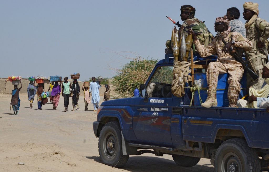 People from the Nigerian town of Malam Fatori an its area, close to the borders with Niger and Chad, pass by a car with Chadian Gendarmes (in uniform) as they flee Islamist Boko Haram attacks to take shelter in Niger. Photo courtesy of Issouf Sanogo/AFP/Getty Images.