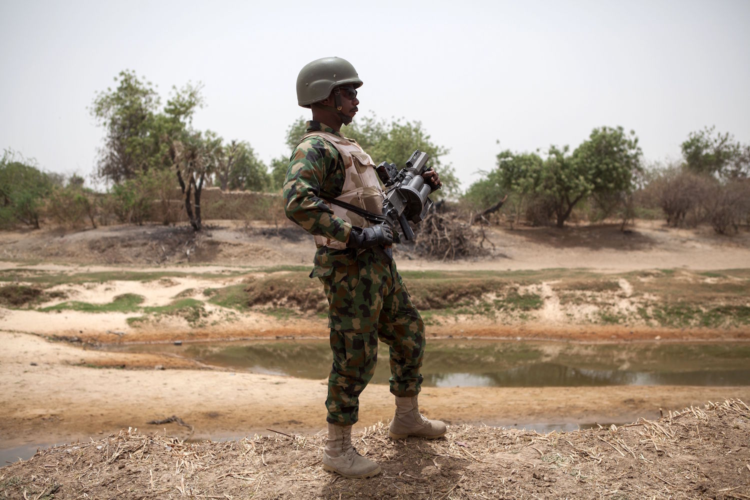 A Nigerian soldier, with a grenade launcher, stands guard near the Yobe river, that separates Nigeria from Niger, on the outskirt of the town of Damasak in North East Nigeria on April, 25 2017 as thousands of Nigerians, who were freed in 2016 by the Nigerian army from Boko Haram insurgents, are returning to their homes in Damasak. Photo courtesy of Florian Plaucheur/AFP/Getty Images.