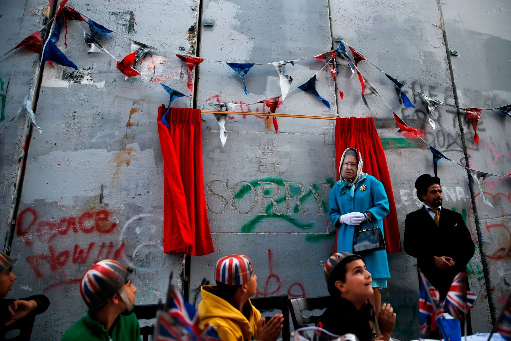 An actor dressed up as Queen Elizabeth and Palestinian children from the al-Aida refugee camp attend an event held by secretive British street artist Banksy to apologise for the 100th anniversary of the Balfour Declaration on November 1, 2017 at his Walled-Off Hotel in Bethlehem in the occupied West Bank. Photo by Ahmad Gharabli/AFP/Getty Images.