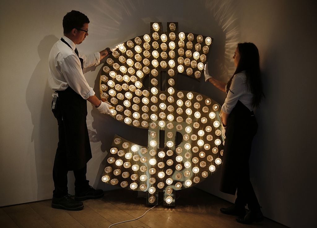 Sotheby's employees pose with a piece of artwork entitled $ by artists Tim Noble and Sue Webster. Image courtesy Adrian Dennis//AFP/Getty Images.
