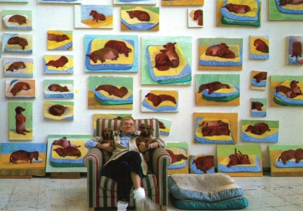 David Hockney and his pet dachshunds Stanley and Boodgie photographed in front of some of the artist's many artworks based on the dogs. Courtesy of Thames and Hudson.