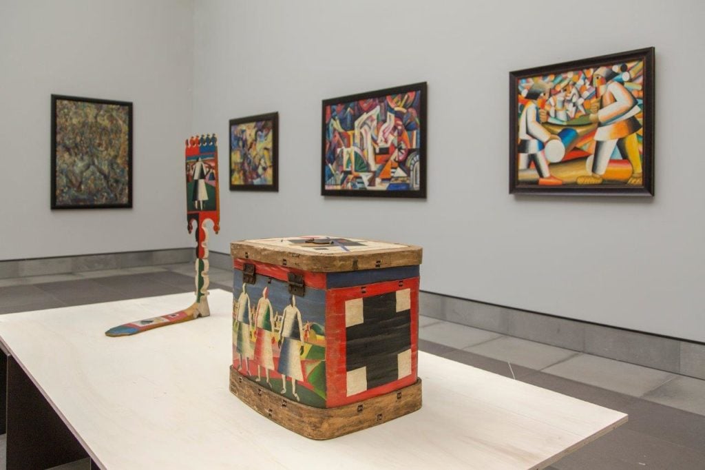 Foreground: Objects including a box and distaff, allegedly decorated by Kazimir Malevich. Background, from left: paintings by Pavel Filonov, Yury Annenkov, Aleksandra Ekster, and Kazimir Malevich. Image courtesy of the Museum of Fine Art in Ghent.