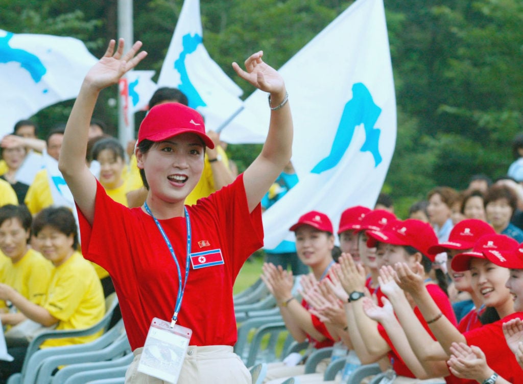 North Koreans (red shirts) cheer as South Koreans (yellow shirts) wave unified Korean peninsula flags during a welcome ceremony at the World Student Games August 21, 2003 in Daegu, South Korea. Photo courtesy of Chung Sung-Jun/Getty Images.