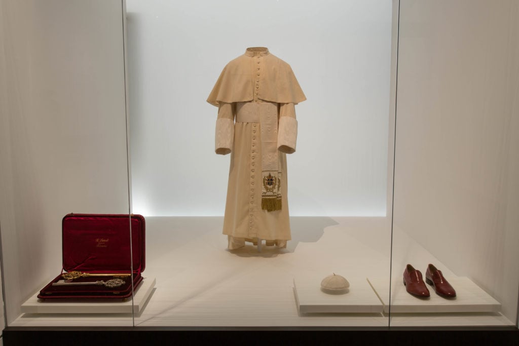 Installation view, featuring St. John Paul II's red shoes, of "Heavenly Bodies" at the Met Fifth Avenue, Lizzie and Jonathan Tisch Gallery, Anna Wintour Costume Center. On loan from the collection of the Liturgical Celebrations of the Supreme Pontiff, Papal Sacristy, Vatican City. Photo courtesy of the Metropolitan Museum of Art. 