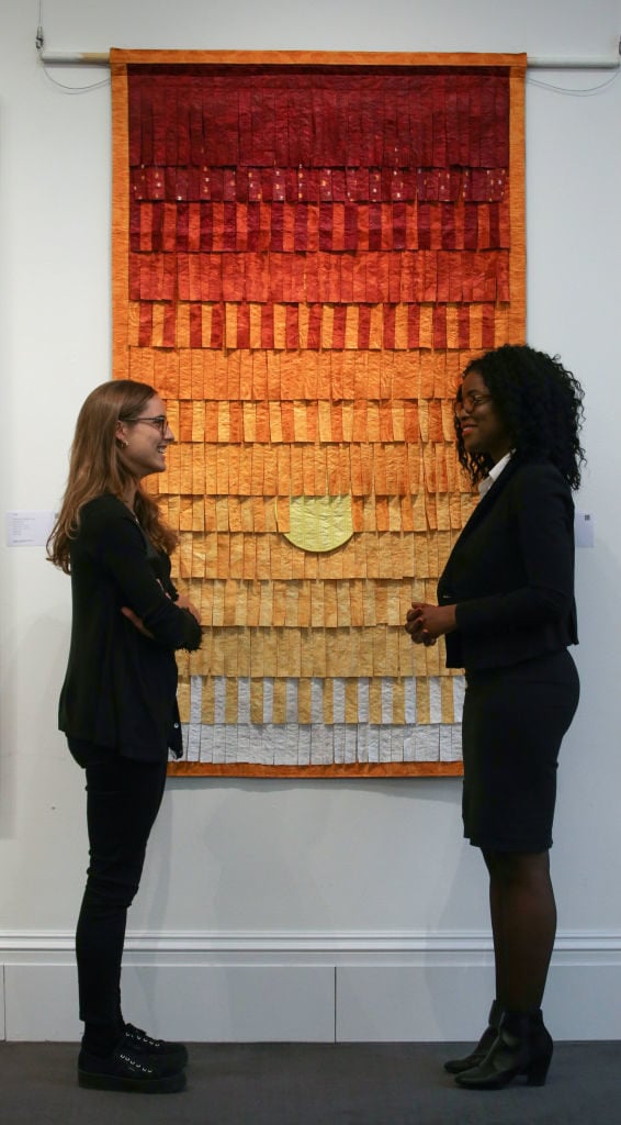 Employees pose with an artwork entitled <em>Composition No. 25 (soleil)</em> (2015), by Malian artist, Abdoulaye Konate with an starting price of 10,000-15,000 dollars / 12,500-18,700 dollars during a photocall to promote the forthcoming inaugural 'Sale of Modern and Contemporary African Art' at Sotheby's in London on May 12, 2017. Photo courtesy Daniel Leal-Olivas/AFP/Getty Images.