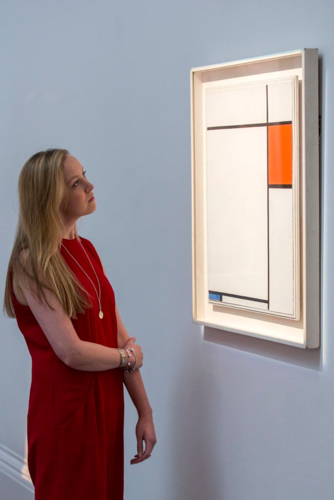 A member of Sotheby's staff poses with Piet Mondrian's 1927 piece <em>Composition with Red, Blue and Grey</em>, estimated to sell for between £13-£18 million, on display at Sotheby's auction house on June 18, 2014 in London, England. Photo by Rob Stothard/Getty Images.