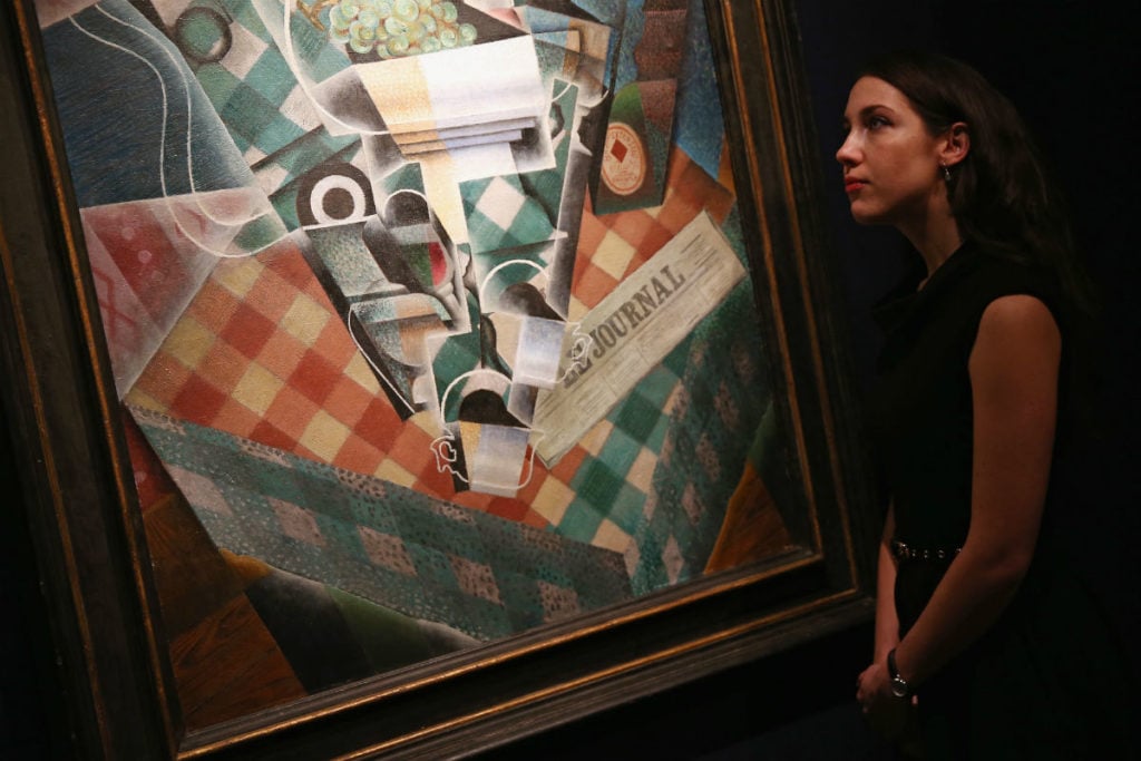 A Christie's employees pose besides a piece of work entitled <em>Nature morte a la nappe a carreaux</em> by Juan Gris at Christie's auction House on January 30, 2014 in London, England. Photo by Dan Kitwood/Getty Images.