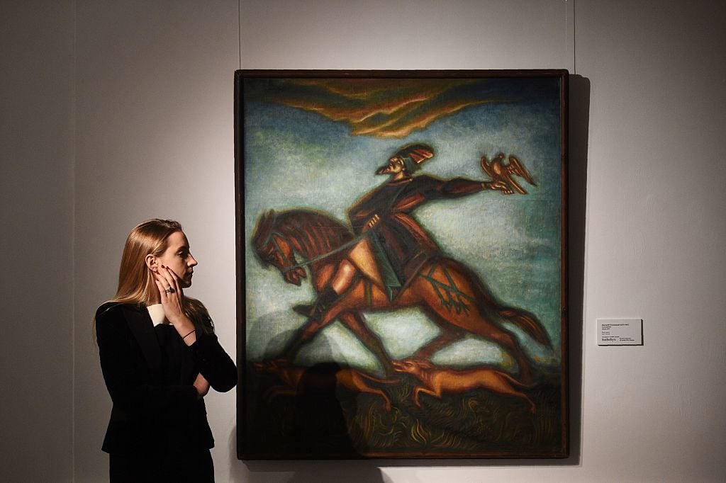 A woman stands by the painting <em>The Hunter</em> by Dmitri Stelletsky during a preview of Sotheby's forthcoming Russian Pictures Including the Bar-Gera Collection of Soviet Non-Conformist Art Sale in London, in Moscow on November 2, 2016. Photo credit Natalia Kolesnikova/AFP/Getty Images.