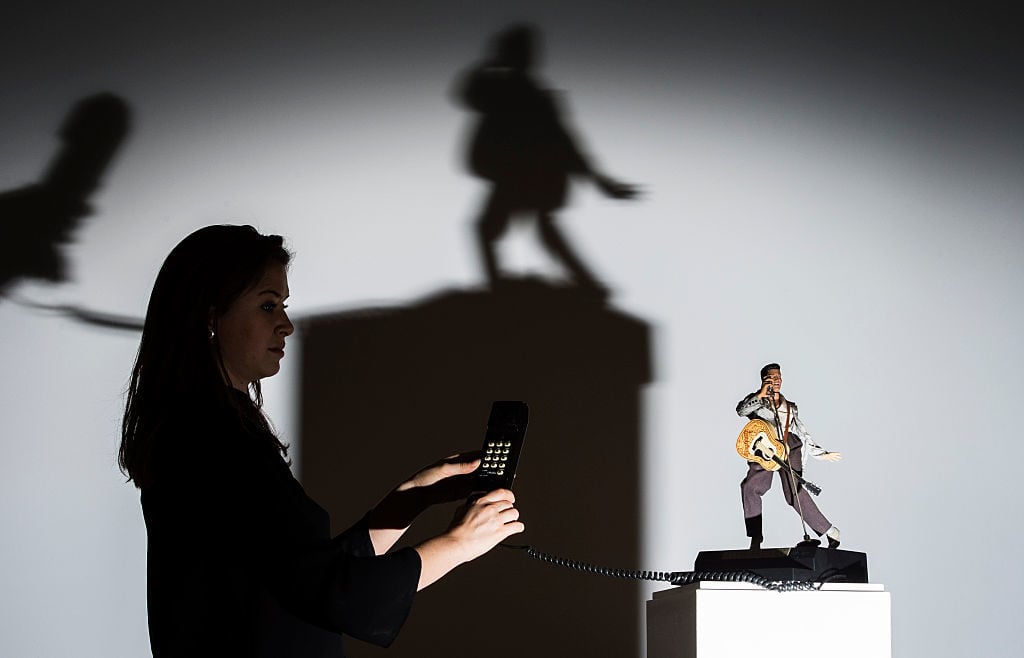 A Sotheby's employee stands with a novelty Elvis telephone during the pre-auction preview of the personal collection of Deborah Cavendish, Duchess of Devonshire at Sotheby's on February 26, 2016 in London, England. Photo by Justin Setterfield/Getty Images.